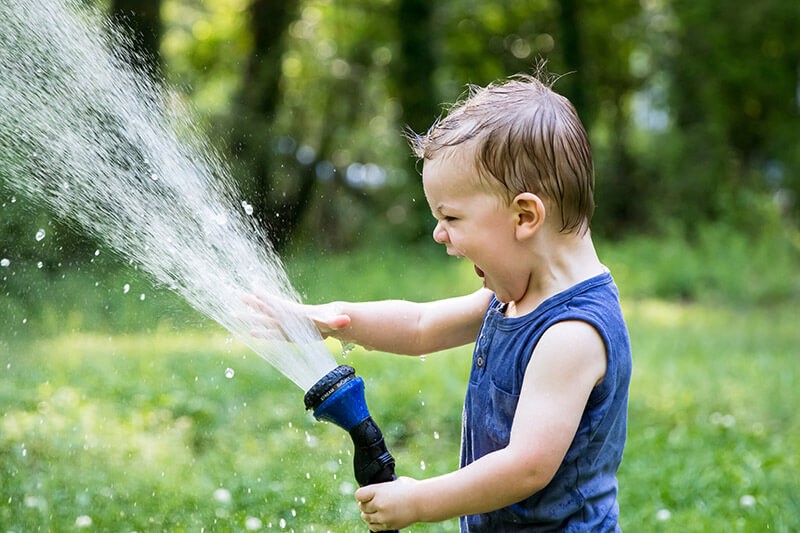 a young boy sprays a water hose in a yard